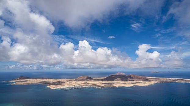 Breathtaking aerial view of La Graciosa Island with vibrant blue skies and fluffy clouds.