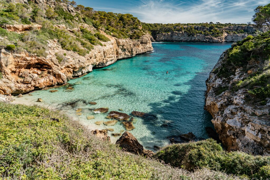 Explore a tranquil bay with clear turquoise waters and rugged cliffs in Palma, Spain. Perfect for travel inspiration.